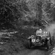 A black and white photo of a vintage car driving on a snow-covered trail.